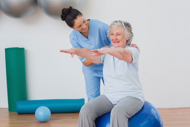 Imagem de uma fisioterapeuta auxiliando uma paciente idosa durante um exercício de equilíbrio